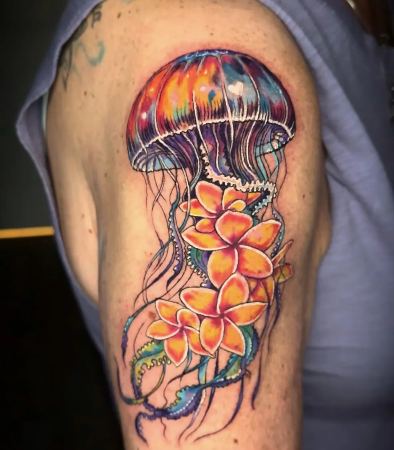 Color tattoo of a jellyfish with orange plumeria flowers, on an upper arm