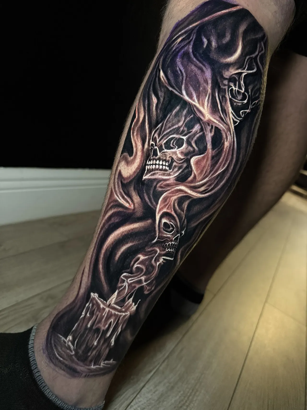 Black and grey realism tattoo of a skull in smoke above a candle, on a calf