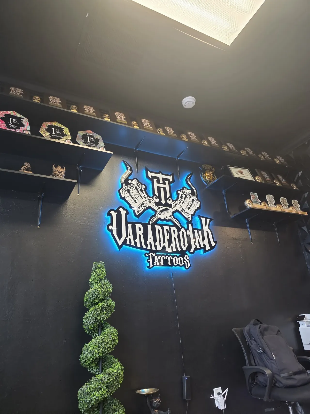 Varadero Ink studio wall with the blue neon sign, black panels and a trimmed topiary